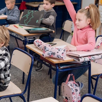Criança sentada numa sala de aula com mochila e estojo rosa da Minnie Mouse