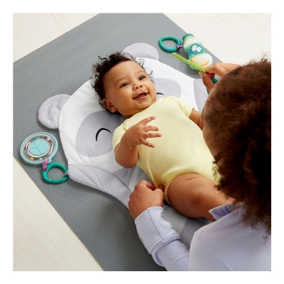 Bebé deitado em manta com rosto de urso, brincando com uma pessoa que segura brinquedos coloridos