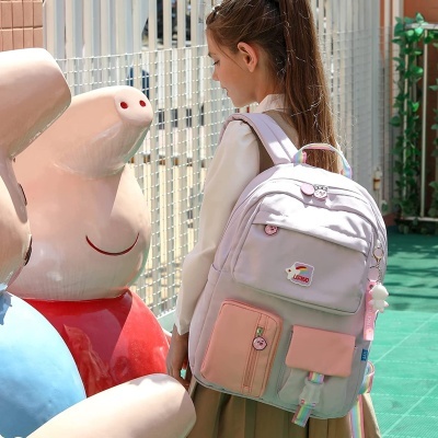 mochila escolar colorida com vários bolsos e acessórios usada por rapariga perto de estátua Peppa Pig