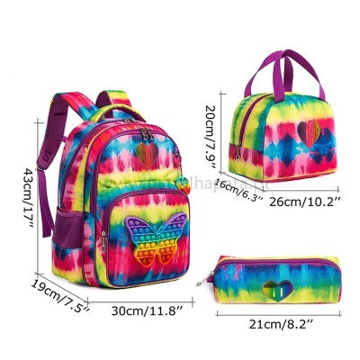 Conjunto de mochila, mala e estojo coloridos com padrão tie-dye e apliques de borboleta e coração.