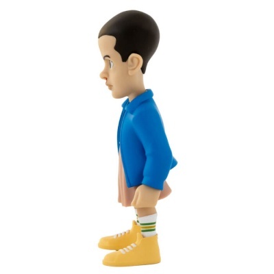 Boneco de vinil vestido com casaco azul e sapatos amarelos, visto de perfil em fundo branco