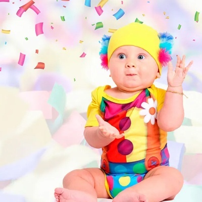 Bebé com roupa colorida e gorro amarelo com pompons em fundo claro com confetes