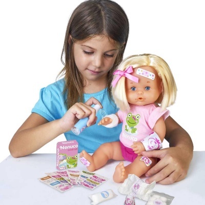 Menina a brincar com uma boneca Nenuco e acessórios médicos em cima de uma mesa branca.