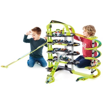 Crianças a brincar com um conjunto infantil de parque de estacionamento e rampa para carrinhos em plástico verde e preto.