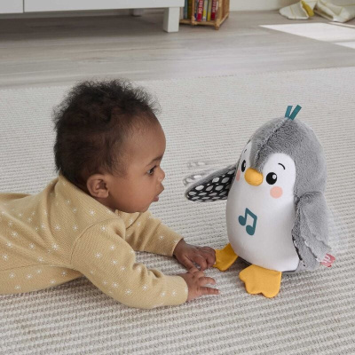 Pelúcia de pinguim cinza e branco com detalhes amarelos e azuis sobre tapete cinza e criança ao lado