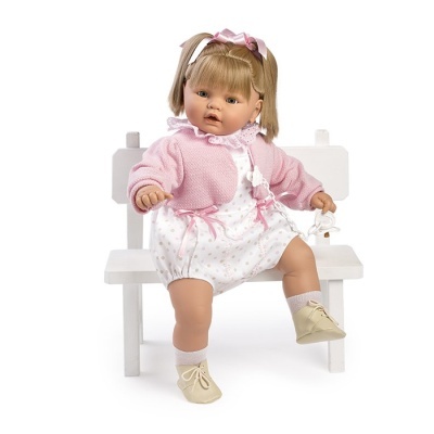 Boneca bebé vestida de rosa sentada num banco branco, segurando um chupa