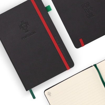 Três cadernos pretos com elásticos e fitas, um aberto com páginas pautadas e brasão na página.