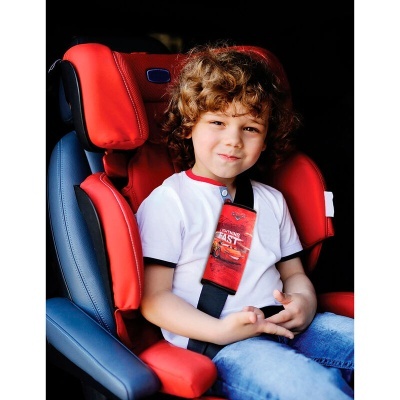 Criança numa cadeira automóvel vermelha e azul com cinto de segurança e almofada vermelha com desenho