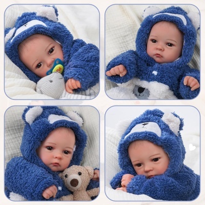 Bebé realista em fato de pelúcia azul com capuz de urso, segurando peluche e chupeta