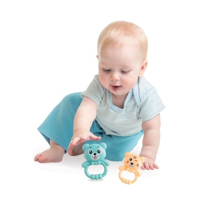 Bebé loiro brincando com mordedores de plástico azuis e amarelos no chão branco