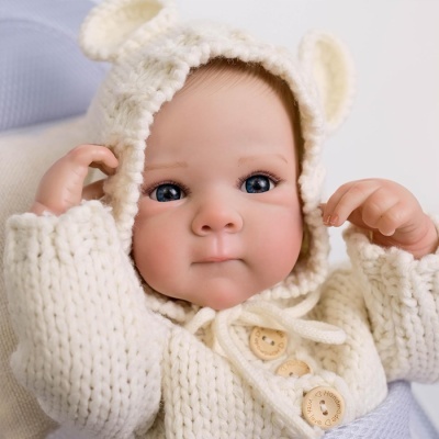 Boneca bebé realista com casaco de malha branco e capuz com orelhas.