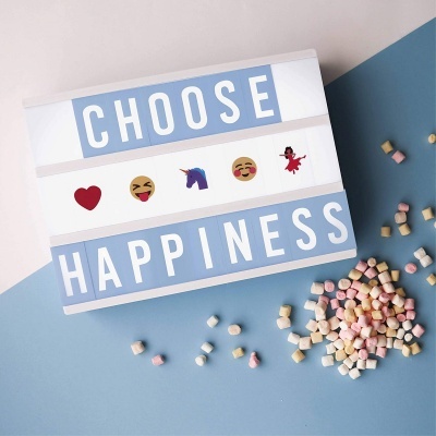 Caixa luminosa branca com bordas azuis, texto CHOOSE HAPPINESS e emojis, com marshmallows coloridos ao lado