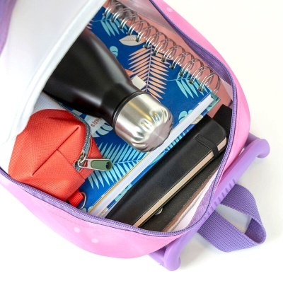 Mochila rosa aberta com caderno azul de folhas decoradas, garrafa preta metálica, estojo vermelho e tablet preto dentro.