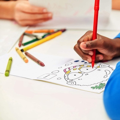Mesa com desenho de boneco de neve sendo colorido com marcador vermelho e canetas de cera ao redor.