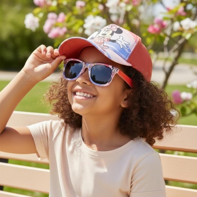 Criança com óculos de sol estampados da Minnie e boné coral sentado num banco ao ar livre