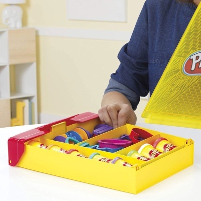 Recipiente amarelo com massas Play-Doh e ferramentas, pessoa com camisa azul a abrir
