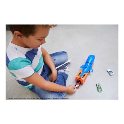 Brinquedo azul e laranja com dois carrinhos de brinquedo no chão cinzento e criança sentada.