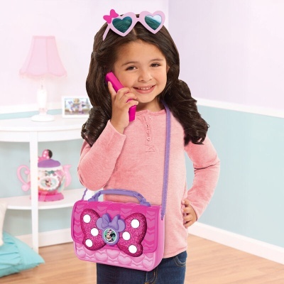 Menina com roupa rosa segurando telemóvel e mala rosa com figura da Minnie Mouse