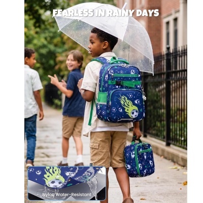 Mochila azul e bolsa térmica com padrão de bolas de futebol e chamas verdes, em uso por menino com guarda-chuva transparente