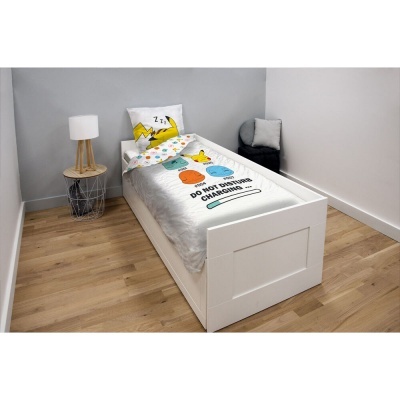 Cama branca com roupa de cama e almofada estampadas, mesa de cabeceira com candeeiro e cadeira num quarto