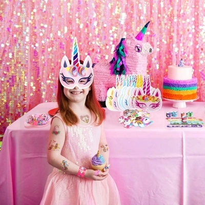 Menina com máscara de unicórnio e vestido rosa segura cupcake em festa com decoração de unicórnio