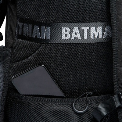 Mochila preta com fita escrita BATMAN e telemóvel no bolso frontal.