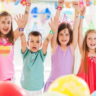 Crianças com roupas coloridas e acessórios de unicórnio numa festa com balões
