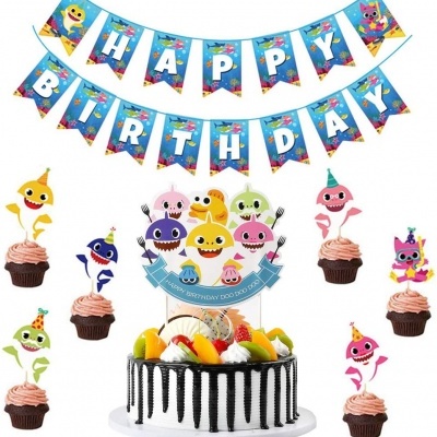 Decorações de aniversário com tema de tubarão: bolo com frutas e topper, faixa 'HAPPY BIRTHDAY' e cupcakes com figuras de tubarão.