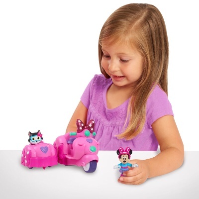 Menina a brincar com brinquedos rosados em forma de mota com sidecar e figuras de personagens.