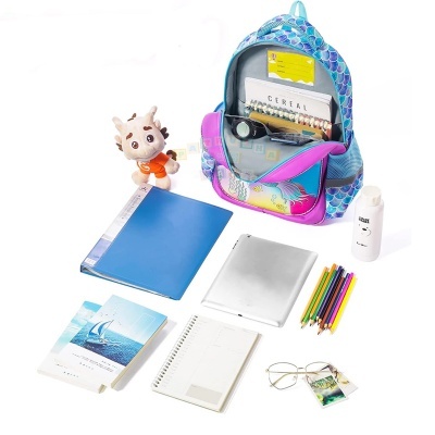 Mochila azul e rosa com padrão de escamas e vários objetos escolares espalhados.