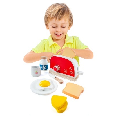 Criança loira com camisa amarela brinca com brinquedo de cozinha e torradeira vermelha em fundo branco