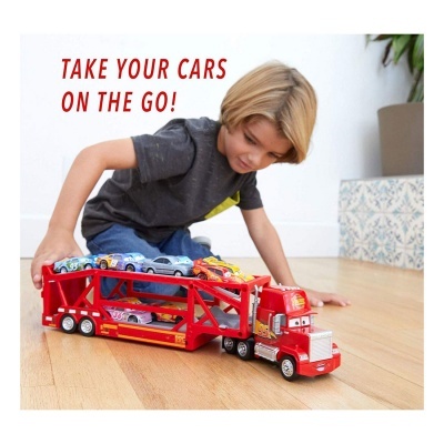 Criança loira brinca com camião de transporte de carros vermelho em chão de madeira