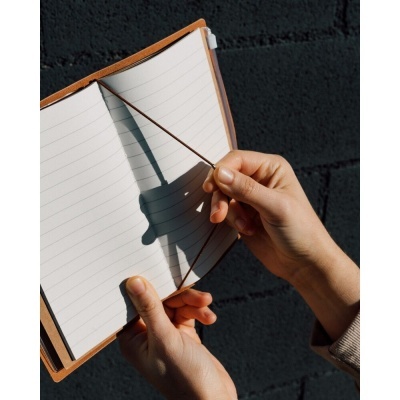 Caderno com capa castanha aberta e mãos segurando