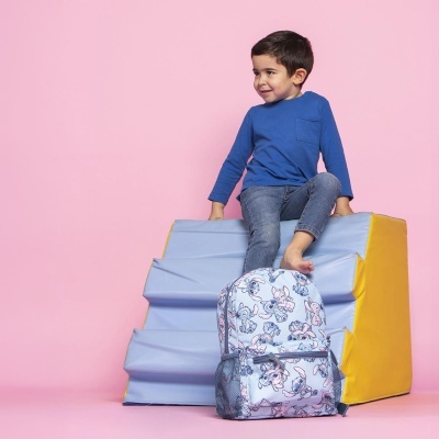 Criança sentada em brinquedo macio azul e amarelo com mochila de padrão cinzento e personagens