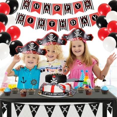 Três crianças com chapéus de pirata em festa de aniversário com bolo e decoração temática