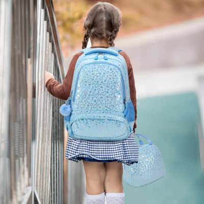 Mochila azul clara com padrão de corações e detalhes brilhantes usada por criança com tranças e roupa azul e castanha