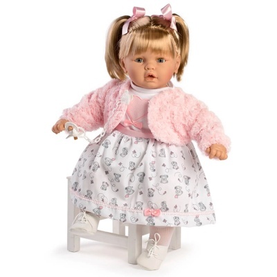 Boneca vestida com casaco rosa felpudo e saia branca com padrão, sentada em cadeira branca.