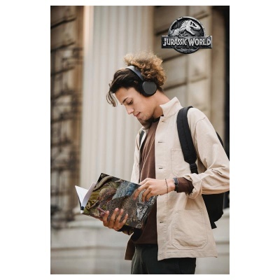 Homem jovem a ler caderno do Jurassic World com auscultadores e mochila