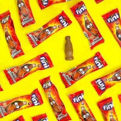Doces em forma de garrafa de cola com embalagens coloridas sobre fundo amarelo