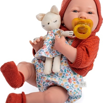 Boneca realista com roupa de malha cor de ferrugem, body e calças justas com padrão floral segurando boneco peluche