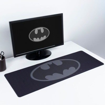 Tapete para rato preto com logótipo do Batman cinza, colocado numa secretária branca ao lado de monitor com o mesmo logótipo no ecrã.