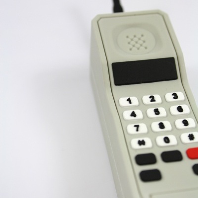 Telefone móvel retro cinzento com botões numéricos e antena sobre fundo branco