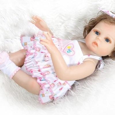 Boneca realista de bebé com vestido e fita rosa, deitada em textura felpuda branca