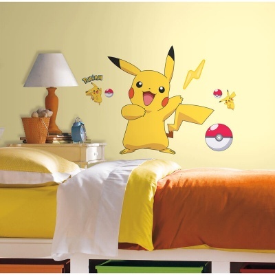 Adesivo de parede colorido do Pikachu e Pokébolas numa parede amarela acima de uma cama com colchas coloridas.