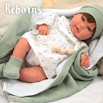Boneca reborn com roupa e manta verdes sobre superfície clara.