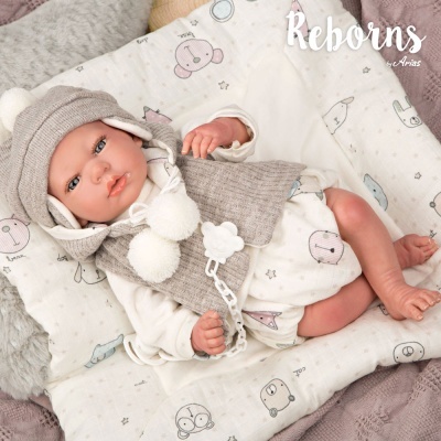 Boneca reborn vestida com roupa bege e branca deitada em almofada acolchoada com desenhos de animais