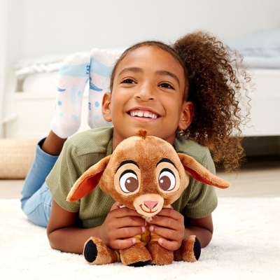Criança a sorrir deitada no chão segurando peluche de cão castanho com orelhas compridas