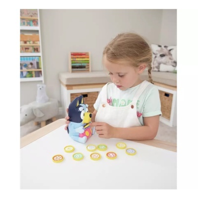 Criança a brincar com figura de cão azul e cartões coloridos sobre mesa branca