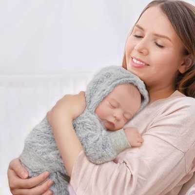 Bebé a dormir vestido de pelúcia cinzenta com capuz, abraçado por mulher com camisola rosa claro.