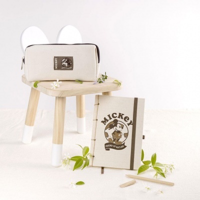 Estojo e caderno Mickey em tecido bege e marrom sobre banco de madeira clara com flores verdes e brancas